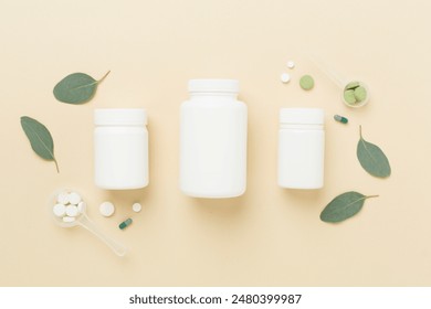 Bottle with pills and green leaves on color background, top view