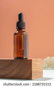 Bottle With Pipette Made Of Dark Amber Glass, Cosmetic Product Wooden Pedestal Coral Background