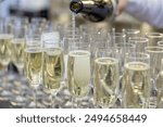 A bottle pours liquid into champagne glasses arranged in a row, suggesting a celebratory event