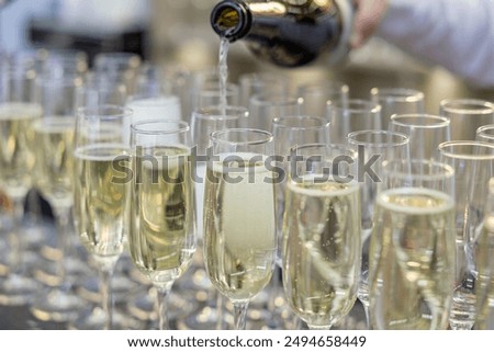 A bottle pours liquid into champagne glasses arranged in a row, suggesting a celebratory event