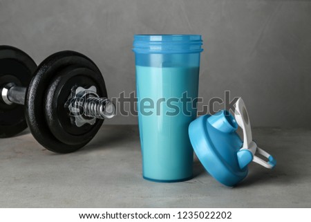 Bottle with protein shake and dumbbell on grey table
