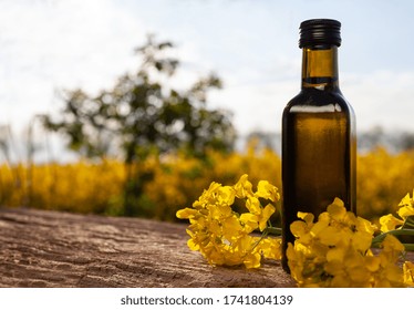 Bottle Of Rapeseed Oil (canola) And Rape Flowers Bunch On Table. Rapeseed Oil On Wooden Table In Field