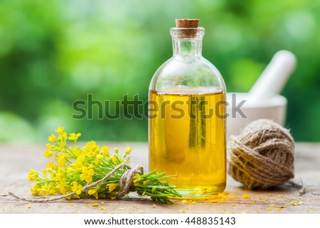 Bottle of rapeseed oil (canola) and rape flowers on table outdoors