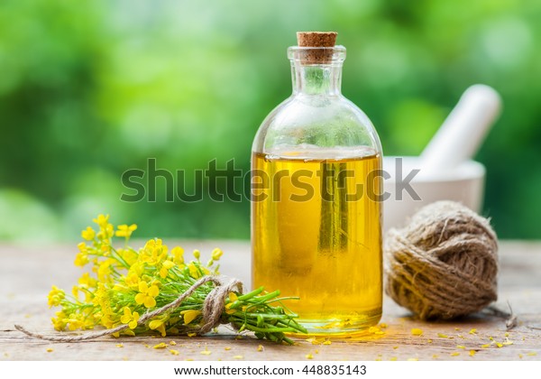 Bottle of rapeseed oil (canola) and rape flowers\
on table outdoors