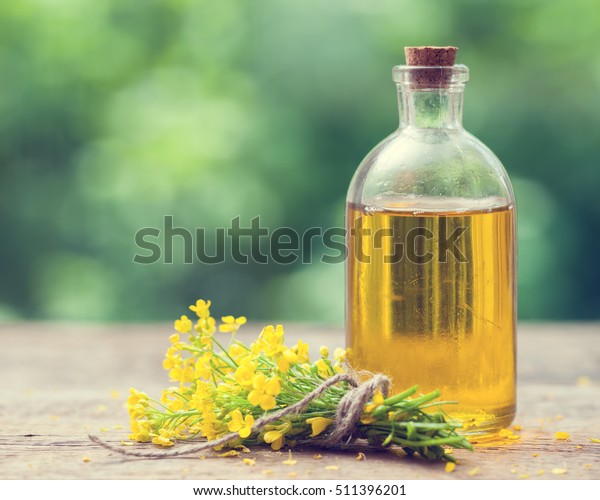 Bottle of rapeseed oil (canola) and rape flowers\
bunch on table outdoors
