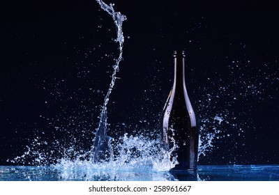 Bottle With Red White Wine, Water Splash, Wine On Table On Dark Black Background, Big Splash Around Bottle Of Red White Wine Splash On Black