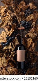 Bottle Of Red Wine With Corkscrew. On A Table Dried Vine Leaves And Blue Grapes. On A Bottle Empty Old Paper Label, Free Space For Your Text.