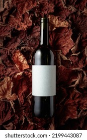 Bottle of red wine with empty label on dried-up vine leaves. Top view.