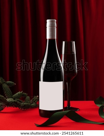 A bottle of red wine with an empty label for the logo and a glass of wine om a Christmas background