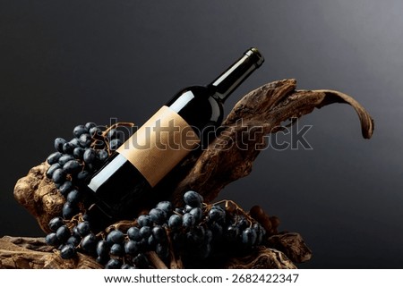 Bottle of red wine with empty label on a old snags. Red wine, grapes, and snags on a black background. Copy space.