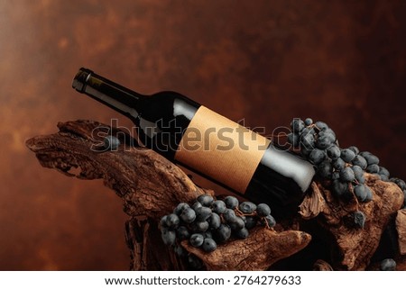 Bottle of red wine with empty label. Unopened bottle of red wine, blue grapes, and old weathered snag. Frontal view with copy space.