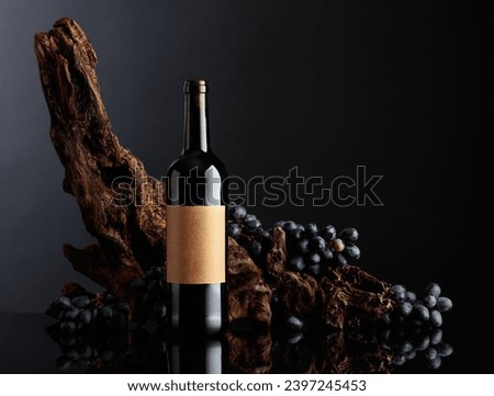 Bottle of red wine with the old empty label. In the background old weathered snag and blue grapes. Copy space.