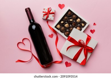 Bottle of red wine on colored background for Valentine Day with gift and chocolate. Heart shaped with gift box of chocolates top view with copy space.