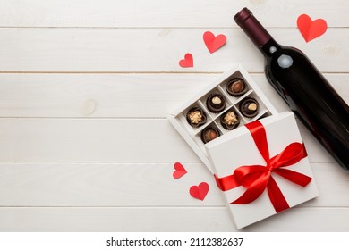 Bottle Of Red Wine On Colored Background For Valentine Day With Gift And Chocolate. Heart Shaped With Gift Box Of Chocolates Top View With Copy Space.
