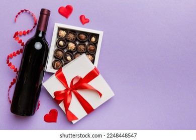 Bottle of red wine on colored background for Valentine Day with gift and chocolate. Heart shaped with gift box of chocolates top view with copy space. - Shutterstock ID 2248448547