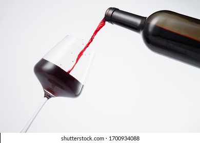 Bottle of red wine poured into the wine glass, on white background. 