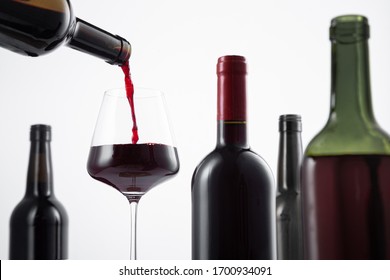 Bottle of red wine poured into the wine glass, and variety of wine bottles with selective focus on  white background.  