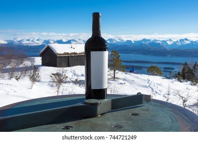 A Bottle Of Red Wine Standing On Steel  Table In Front Of Winter Snow Mountains Background. Molde City, Norway.