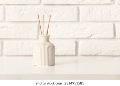 Bottle of reed diffuser on table near light brick wall in room