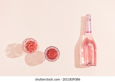 Botella de vino de champán rosa y dos vasos con bebida bajo la luz del sol. Concepto de vacaciones de verano. Foto monocroma rosa, vista superior, espacio de copia. Foto de stock