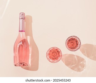 Bottle of rose champagne wine and two glasses with drink in bright sunlight. Summer vacation concept. Pink monochrome photo, top view, copy space.