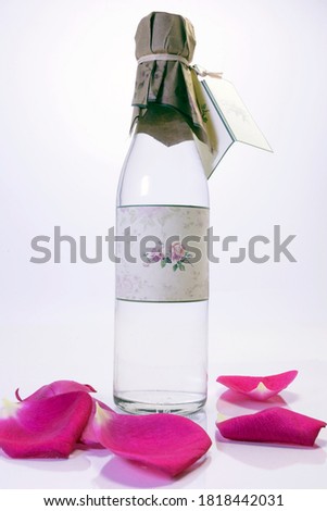 Bottle of rosewater with pink petals of rose flowers