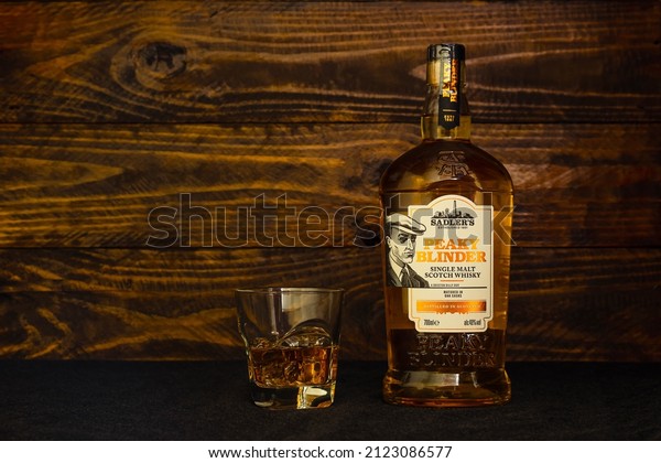 Bottle of Sadler\'s Peaky Blinder Scotch Whisky and a\
glass with ice on a dark wooden background. The Peaky Blinder\
Bourbon reflects the true American spirit. Russia, Krasnodar,\
December 11, 2021