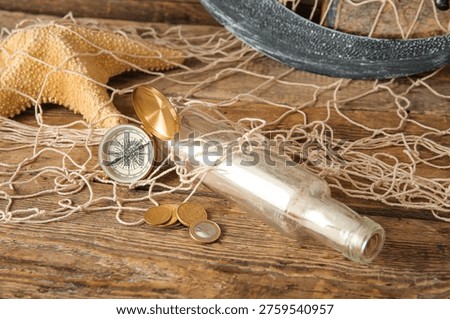 Bottle with scroll, sword, compass and net on brown wooden background