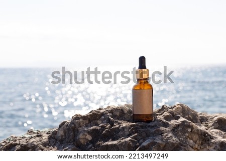 A bottle of serum on the rocks against the sea. A mock-up for a cosmetic product. Skin care essence for beautiful, healthy skin. Blank label