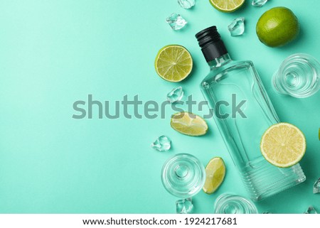 Bottle and shots of vodka, limes and ice on mint background, top view