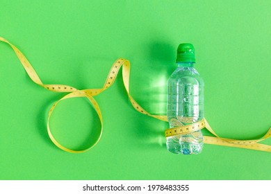 A Bottle Of Still Water And A Measuring Tape On A Green Background. The Concept Of Losing Weight, Healthy Lifestyle, Fasting. Drinking Regime During Exercise, Sports. Duncan's Diet. World Obesity Day.