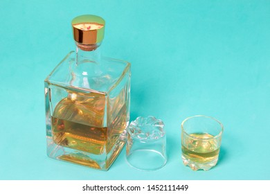 A Bottle Of Strong Alcohol. From Transparent Glass, A Square Form With A Golden Stopper. Near A Stack With A Drink Poured. The Second Stack Is Turned Upside Down. Against The Background Of Mint Color.