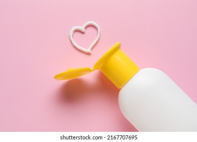 Bottle Of Sunscreen And Heart Made Of Cream On Pink Background