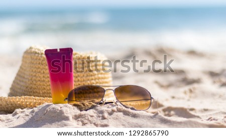 A bottle of sunscreen with sunglasses and panama hat  on a beach, summer skin remedies and protection, vacation at a sea