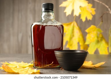 Bottle Of Tasty Maple Syrup, Bowl And Dry Leaves On Light Grey Table