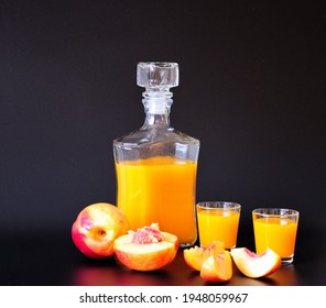 A bottle and two glasses of peach liqueur and sliced ripe fruits on a black background. Close-up.
