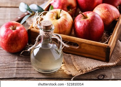 Bottle of unfiltered apple cider vinegar and apples in a wooden box over rustic background close up