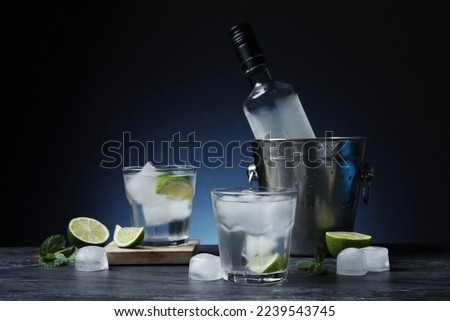 Bottle of vodka, glasses, lime, mint and ice on black marble table