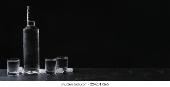 Bottle of vodka and shot glasses with ice on table against black background, space for text. Banner design - Shutterstock ID 2242317265
