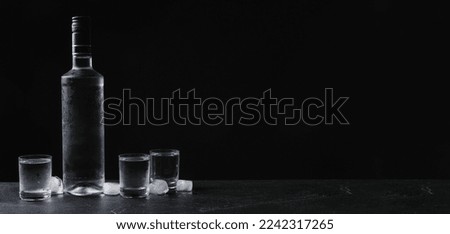 Bottle of vodka and shot glasses with ice on table against black background, space for text. Banner design