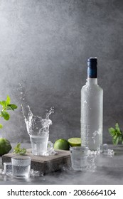 Bottle of vodka with splash shot glass on concrete background with copyspace. Vertical format.