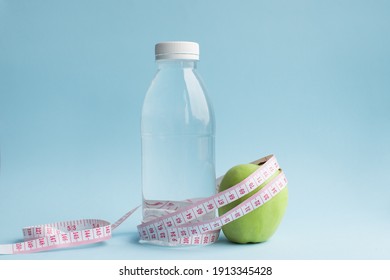 Bottle of water, apple with measuring tape on blue background. Weight loss, counting calories and healthy eating concept - calculate daily nutrition intake. Copy space.
