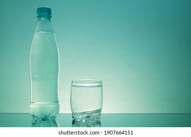 A Bottle Of Water And A Glass Cup Are On A Mirrored Table. Sparkling Water . Plastic Bottle. Gas Bubbles In Water.