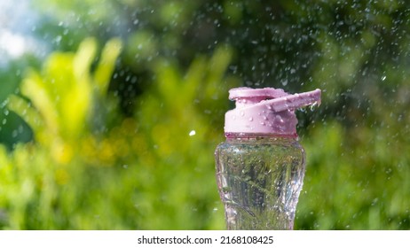 A Bottle Of Water. Reusable Plastic Water Bottle On The Background Of Green Grass. Watered From Above By Raindrops On A Hot Summer Day.