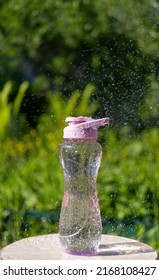 A Bottle Of Water. Reusable Plastic Water Bottle On The Background Of Green Grass. Watered From Above By Raindrops On A Hot Summer Day.