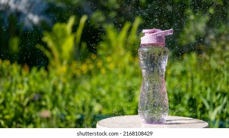 A Bottle Of Water. Reusable Plastic Water Bottle On The Background Of Green Grass. Watered From Above By Raindrops On A Hot Summer Day.