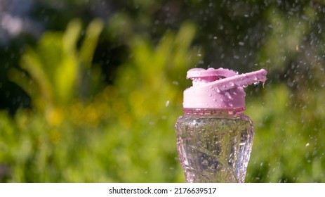 A Bottle Of Water. Reusable Plastic Water Bottle On The Background Of Green Grass. Watered From Above By Raindrops On A Hot Summer Day