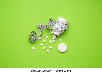 Bottle With Weight Loss Pills And Measuring Tape On Color Background