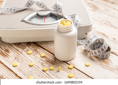 Bottle with weight loss pills, scales and measuring tape on white wooden background