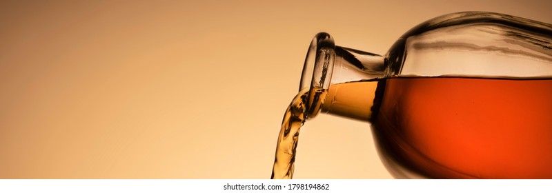 a bottle of whiskey, Bourbon, or liqueur. pouring liquid, a stream from the neck. close - up orange background. panoramic photo, copy space.